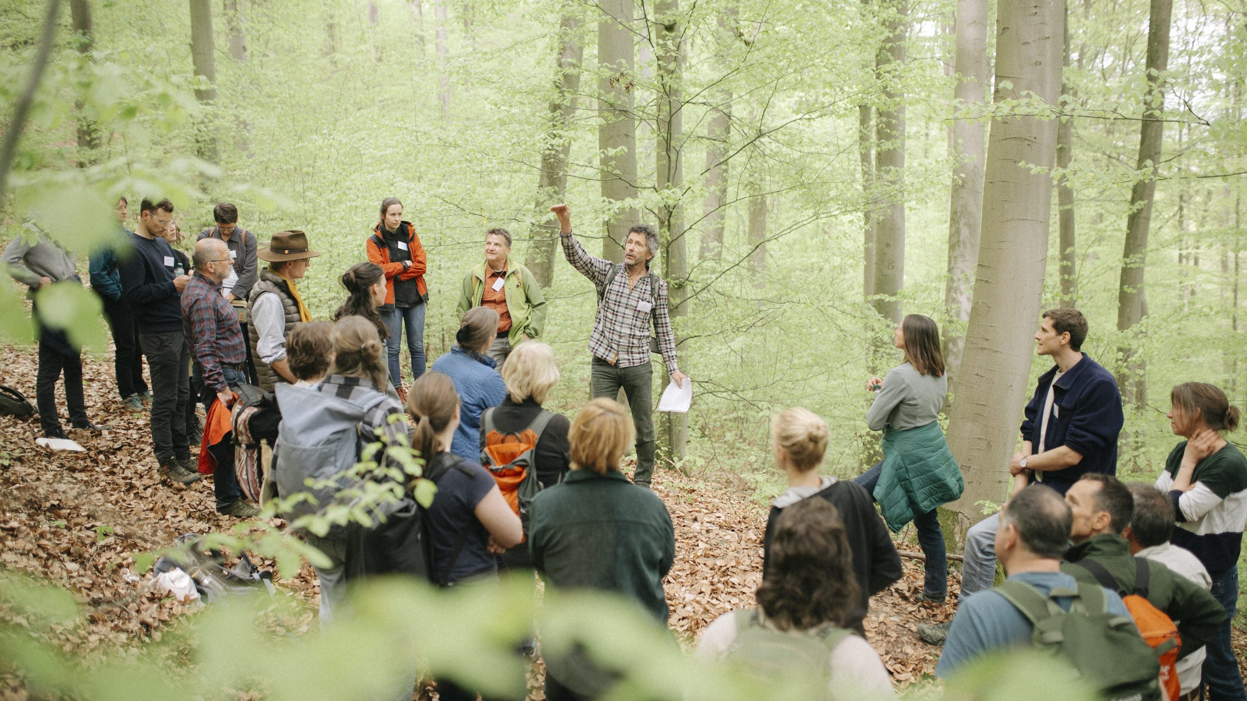 Ein Förster zeigt in den Wald und erklärt einer Gruppe von Menschen etwas